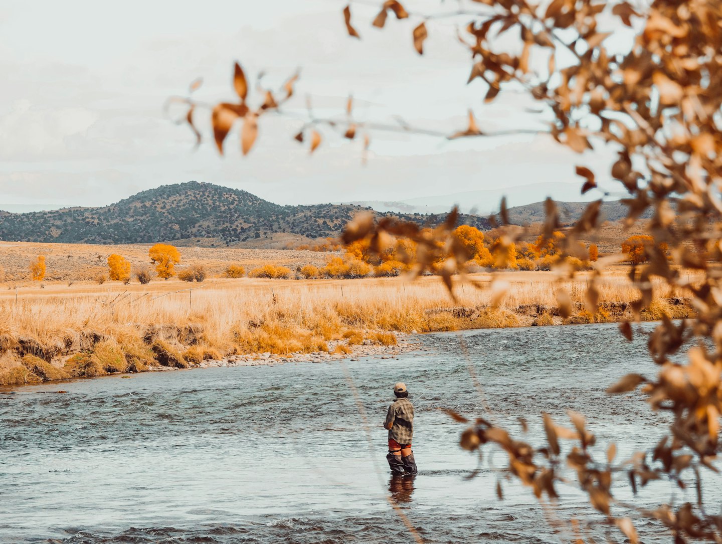 Henkilö perhokalastaa kirkkaassa joessa syksyisten kukkuloiden keskellä.